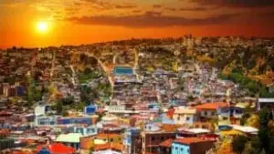 Vista aérea das casas coloridas de Valparaíso ao entardecer, com o sol se pondo no horizonte e céu alaranjado.