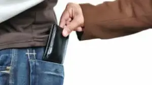 Pessoa sendo furtada com a carteira sendo retirada do bolso traseiro por uma mão sorrateira.