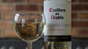 Taça de vinho branco ao lado de uma garrafa Casillero del Diablo Pinot Grigio 2023, com rótulo em destaque e fundo desfocado de tijolos.