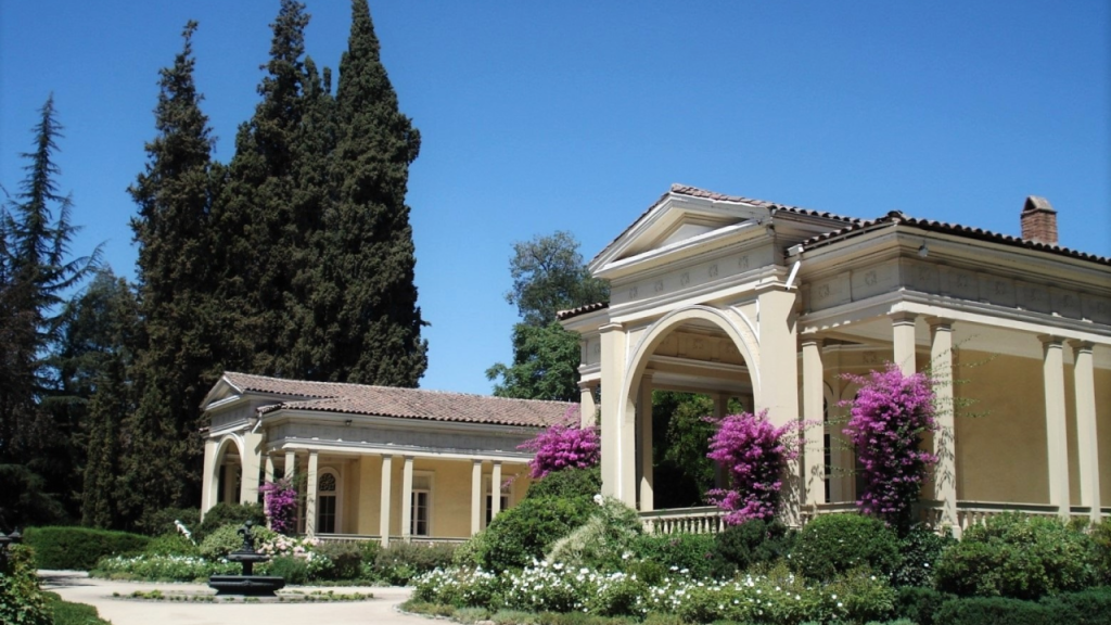 Entrada elegante da vinícola Concha y Toro no Chile, com arquitetura clássica, flores coloridas e árvores ao redor.