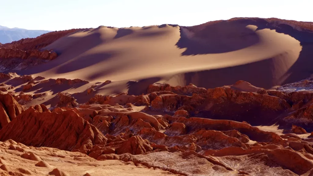 Dunas alaranjadas e formações rochosas no deserto do Atacama sob céu limpo.