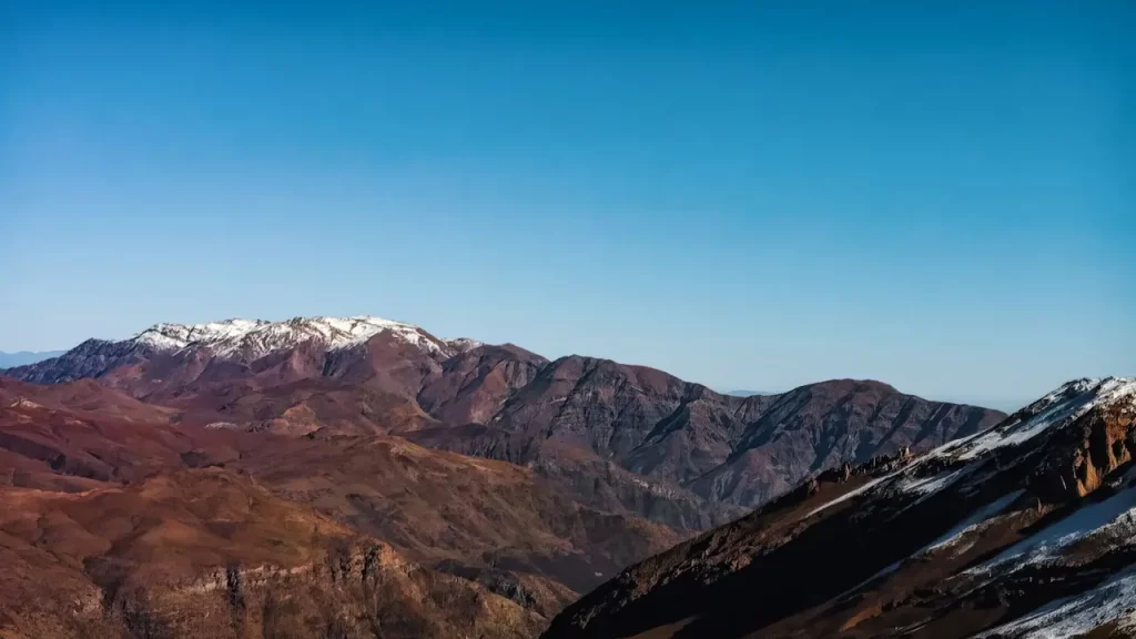 Vista panorâmica da Cordilheira dos Andes com picos nevados e montanhas em tons avermelhados.