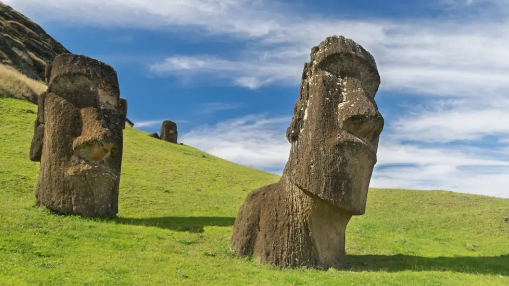 Estátuas moais esculpidas em pedra na Ilha de Páscoa, sobre um gramado verde e céu parcialmente nublado.
