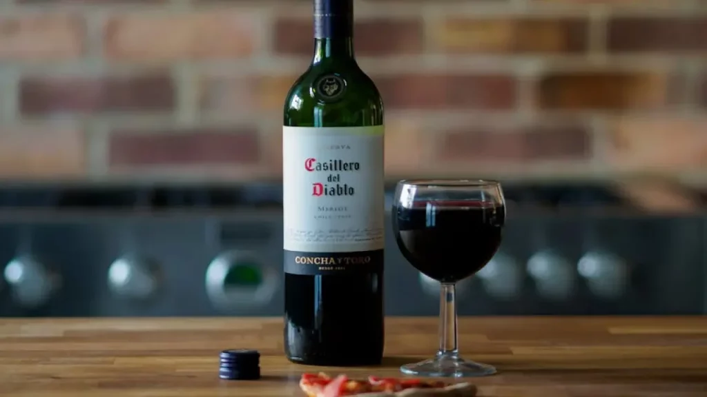 Garrafa de vinho Casillero del Diablo ao lado de uma taça de vinho tinto sobre uma mesa de madeira.