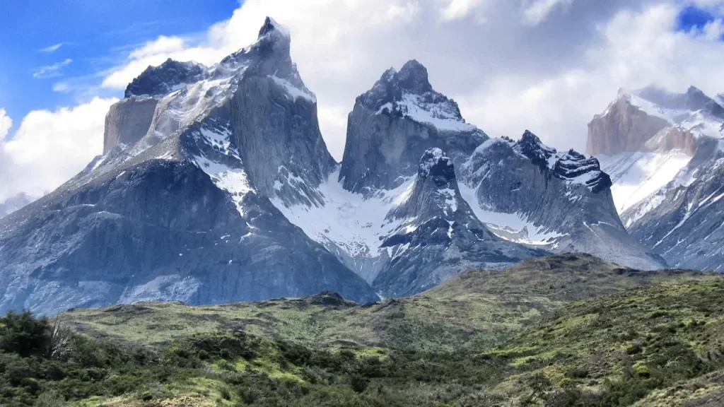 Formações rochosas imponentes das Torres del Paine no sul do Chile, com vegetação verde ao redor.
