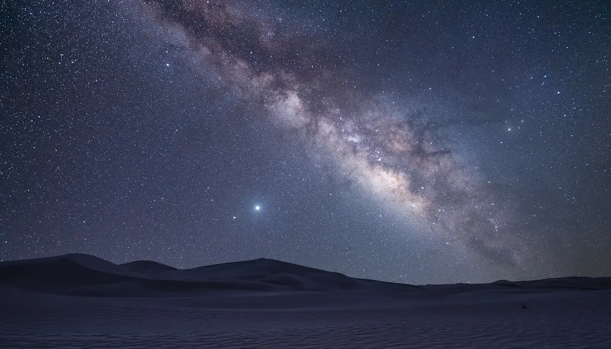 Vista noturna do céu estrelado no Deserto do Atacama, com a Via Láctea brilhando intensamente sobre as dunas.