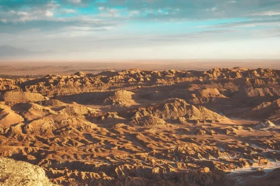 Vista panorâmica do Valle de la Luna no Deserto do Atacama, com formações rochosas esculpidas pela erosão, criando uma paisagem árida e deslumbrante sob um céu parcialmente nublado.