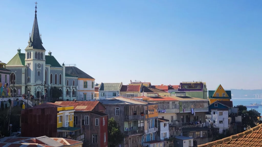 Casas coloridas e a Igreja Luterana em uma colina de Valparaíso, com vista para o Oceano Pacífico em um dia ensolarado.