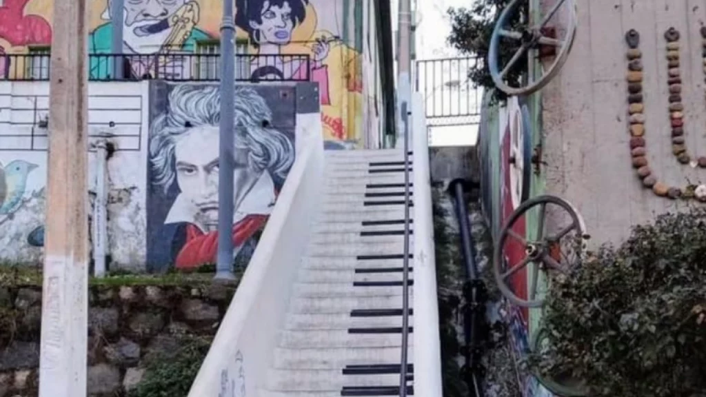 Degraus pintados como teclas de piano na Escadaria do Piano, com murais artísticos ao fundo.