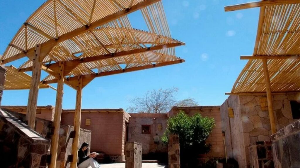 Área comum de um hotel em San Pedro de Atacama, com estrutura de bambu moderna e teto aberto, criando um espaço aconchegante e iluminado.