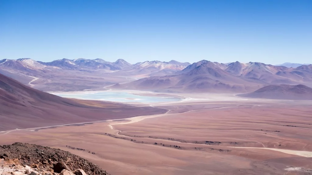 Paisagem árida e deslumbrante do Deserto do Atacama, no Chile, com montanhas ao fundo e céu azul claro.