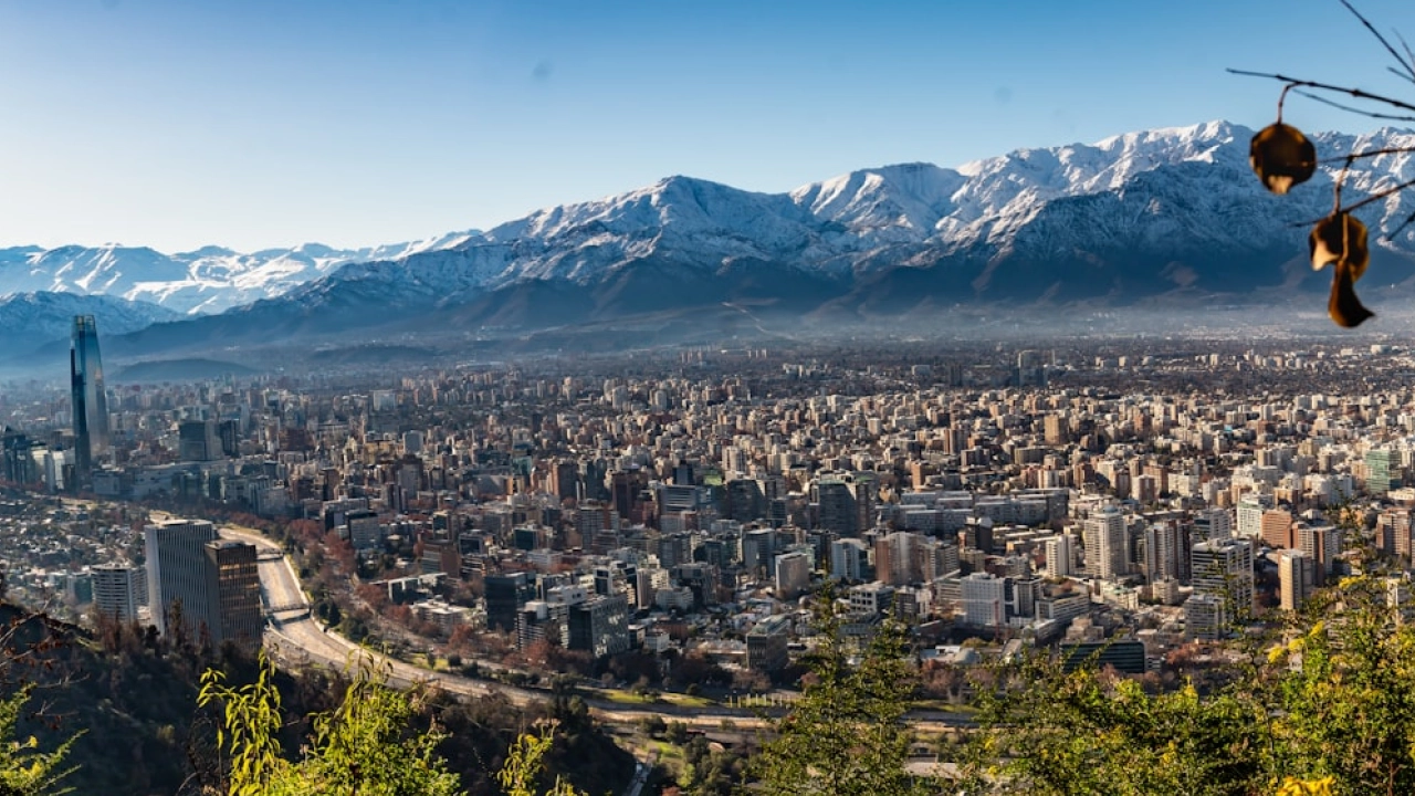 ista panorâmica de Santiago do Chile com a Cordilheira dos Andes coberta de neve ao fundo, capturada de um mirante elevado.