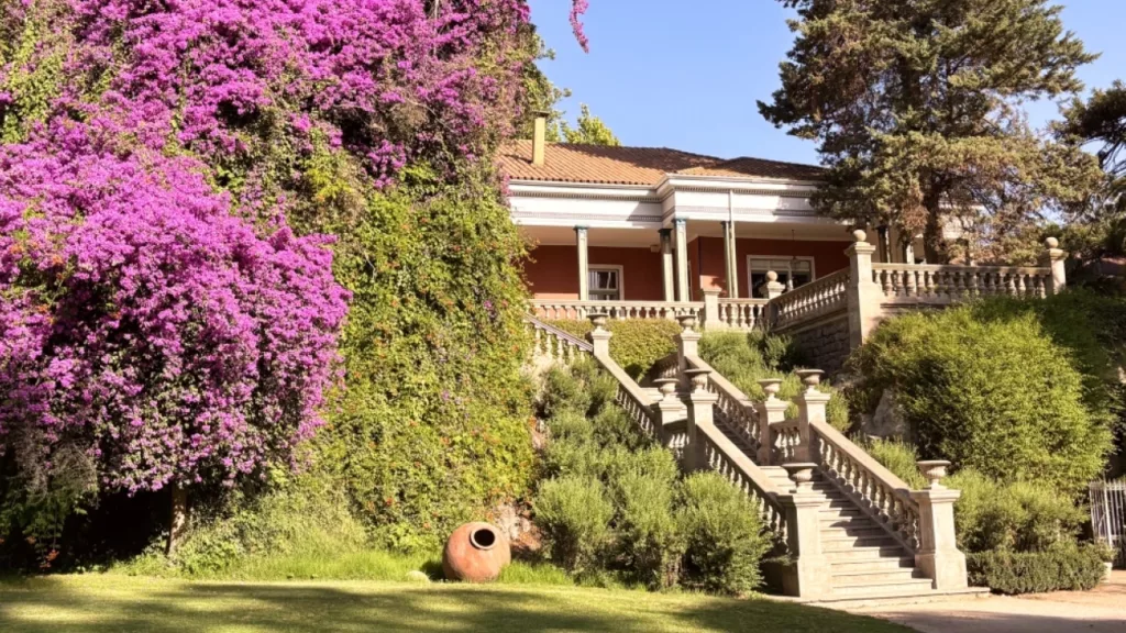 Entrada elegante e rodeada de flores no Hotel Casa Real, localizado na histórica Viña Santa Rita, cercado por jardins exuberantes.