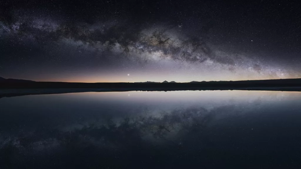 Reflexo perfeito da Via Láctea em uma lagoa no Deserto do Atacama, criando uma paisagem celestial única e deslumbrante.