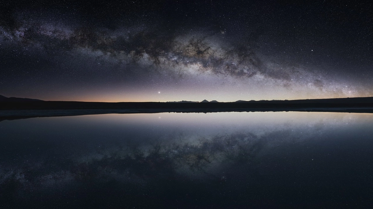 Reflexo perfeito da Via Láctea em uma lagoa no Deserto do Atacama, criando uma paisagem celestial única e deslumbrante.