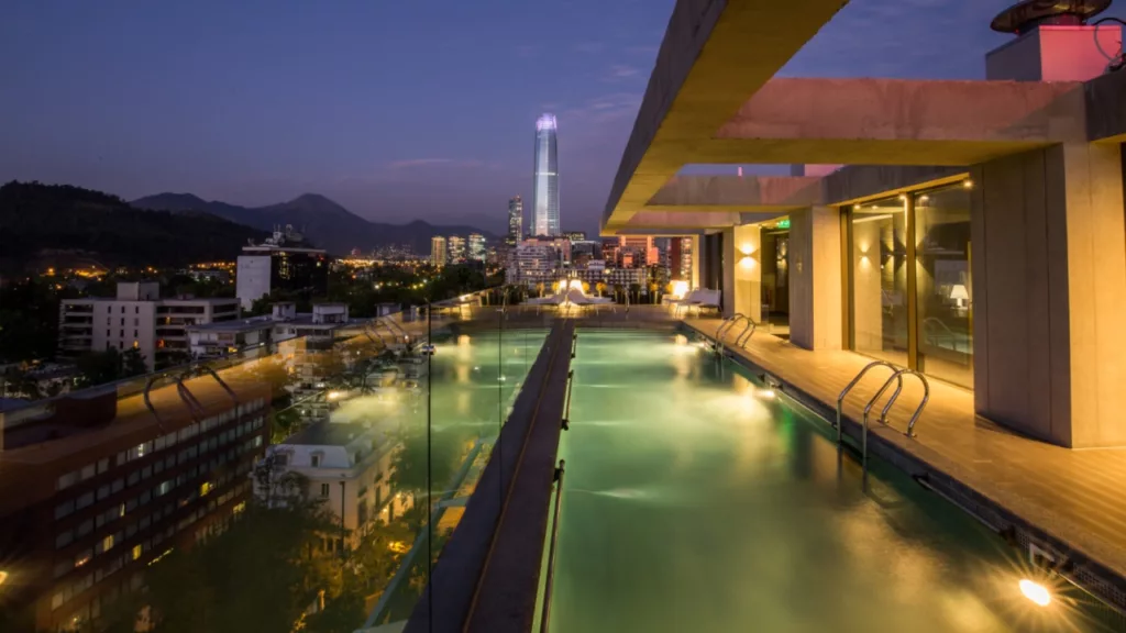 Vista noturna impressionante da piscina na cobertura do Solace Hotel Santiago, com luzes refletindo na água e o skyline da cidade ao fundo.