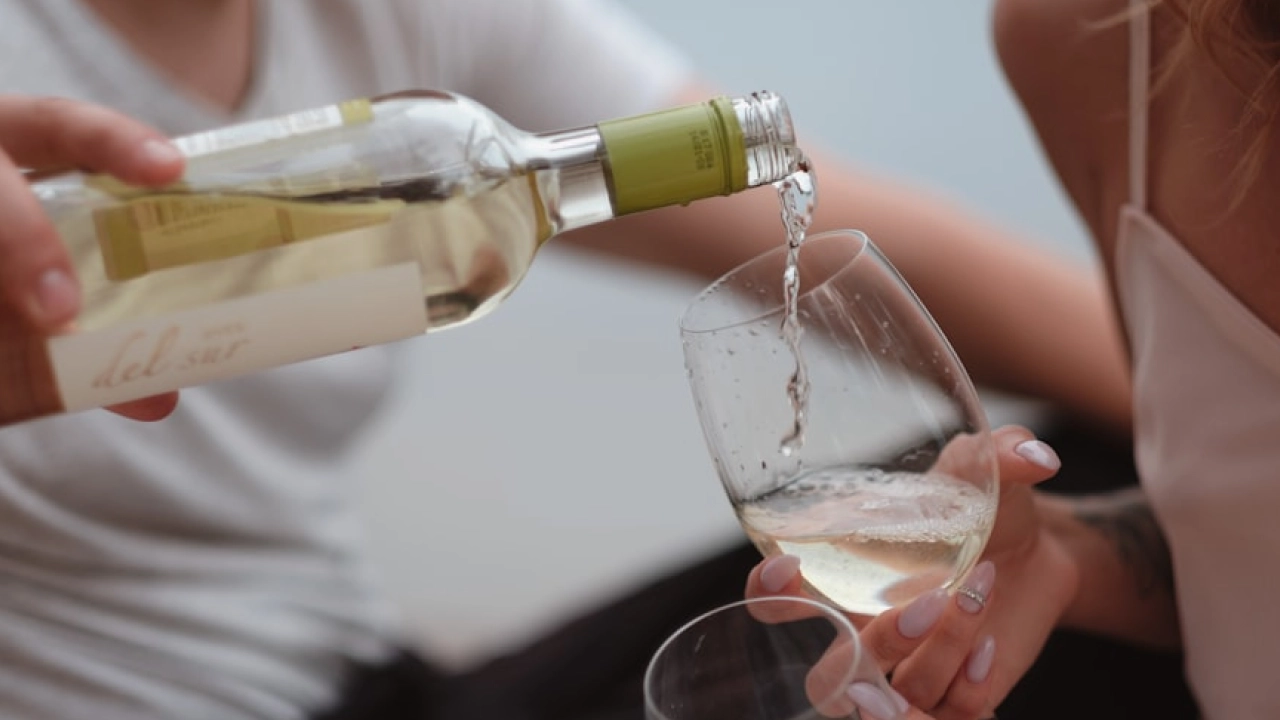 Close-up de um casal brindando com vinho branco chileno, com uma garrafa sendo servida em taças de vidro.