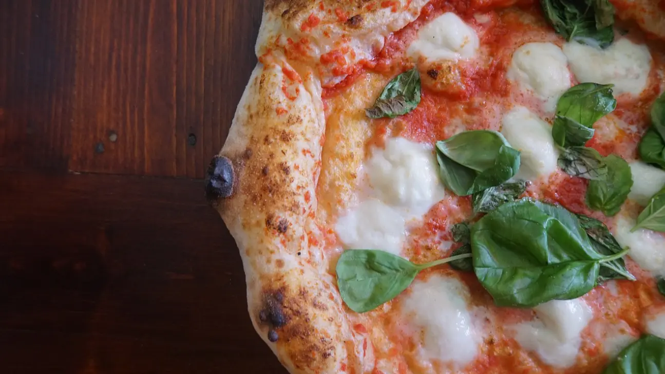 Close-up de uma pizza com molho de tomate, queijo e folhas de manjericão frescas, com a crosta perfeitamente dourada e um toque de azeite.