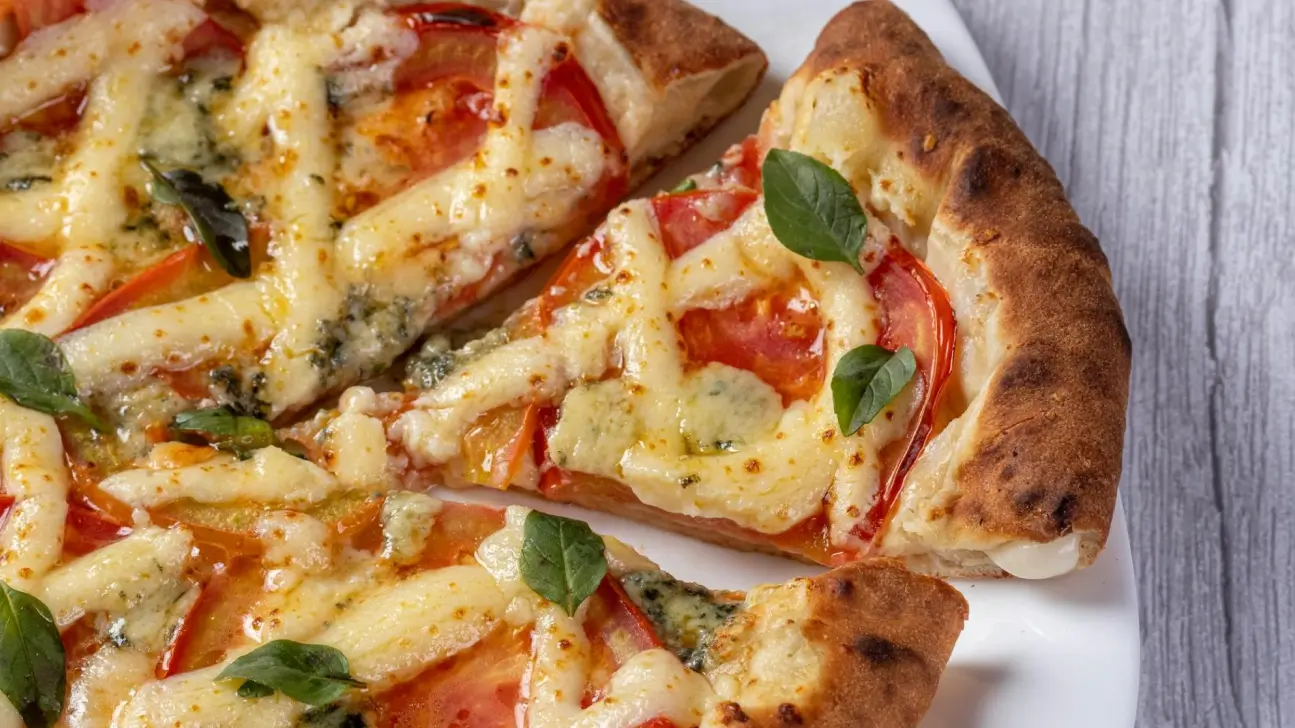 Pizza de tomate e queijo com folhas de manjericão frescas sobre uma base dourada e crocante, com uma fatia já retirada e uma camada de queijo derretido visível.