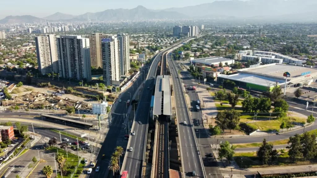 Vista aérea de uma avenida movimentada em Santiago, Chile, com prédios e uma estação de metrô ao centro.