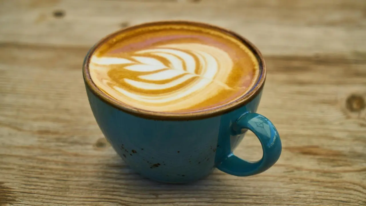 Xícara de café com leite decorado com latte art sobre mesa de madeira, típica de cafeterias em Santiago.