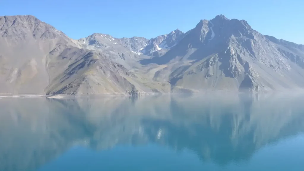 Montanhas refletidas nas águas azul-turquesa do Embalse El Yeso em um dia claro, próximo a Santiago.