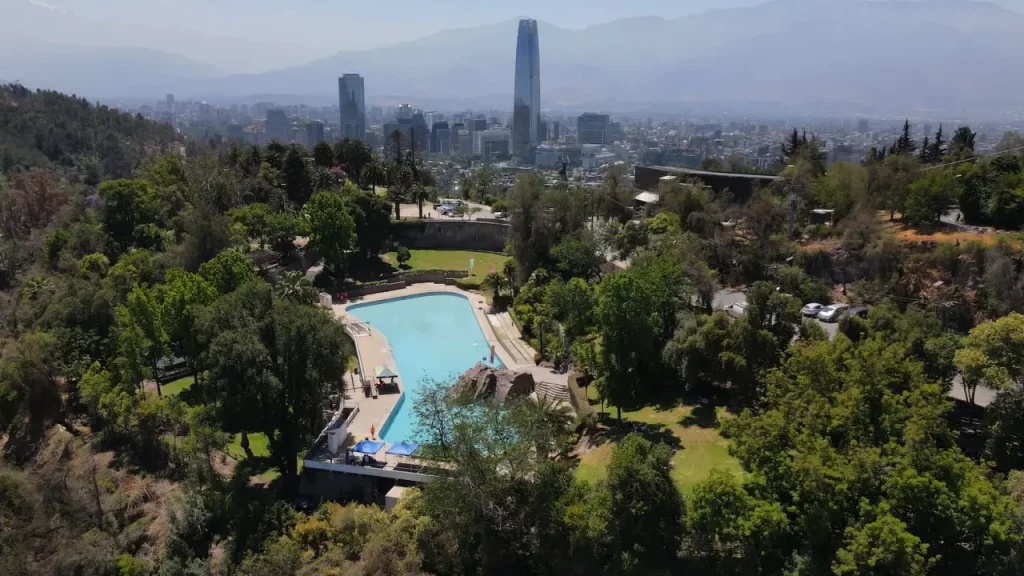Vista panorâmica do Parque Metropolitano de Santiago, com piscina pública, áreas verdes e a cidade ao fundo, incluindo a Cordilheira dos Andes.