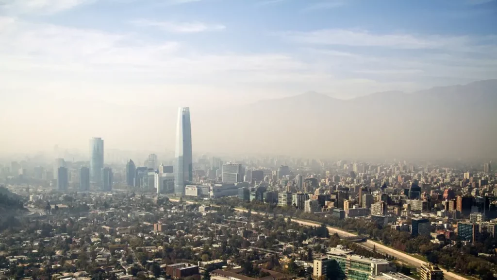 Skyline de Santiago do Chile visto do alto, com destaque para o prédio Costanera Center e as montanhas da Cordilheira dos Andes ao fundo.