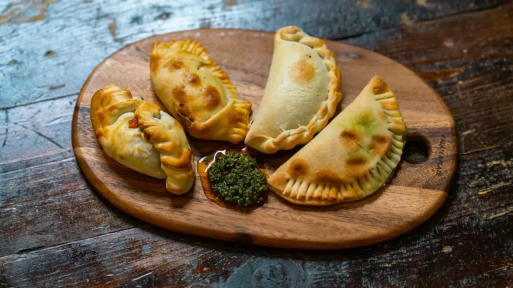 Empanadas chilenas servidas em uma tábua de madeira, acompanhadas de molho verde típico, prato tradicional da culinária do Chile.