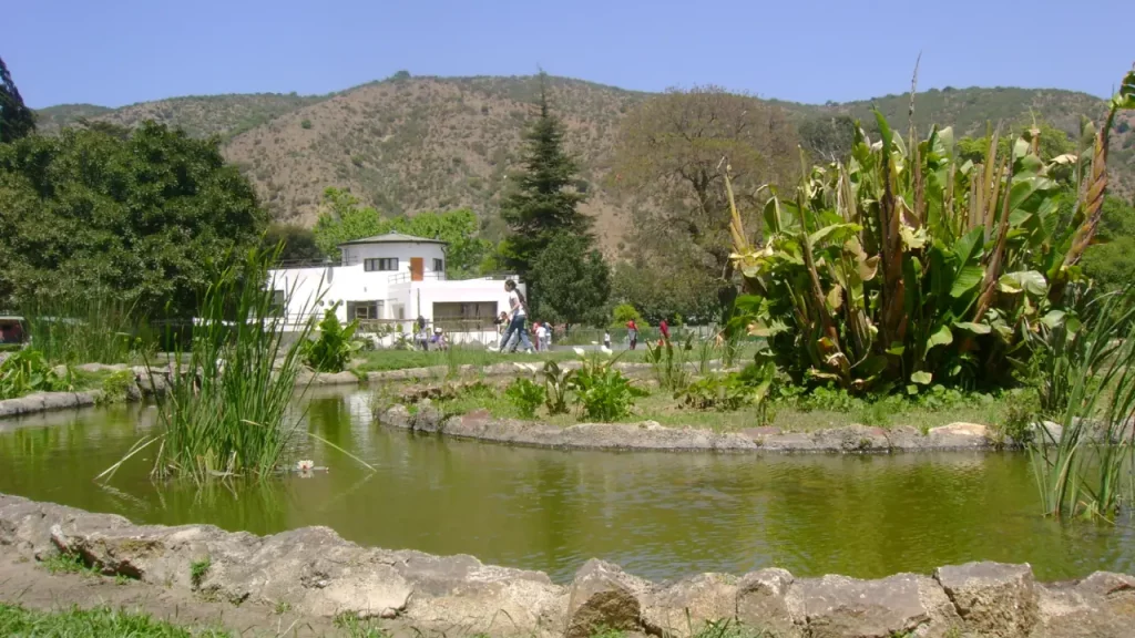 Vista de um lago com vegetação e casa branca ao fundo no Jardim Botânico Nacional de Viña del Mar.