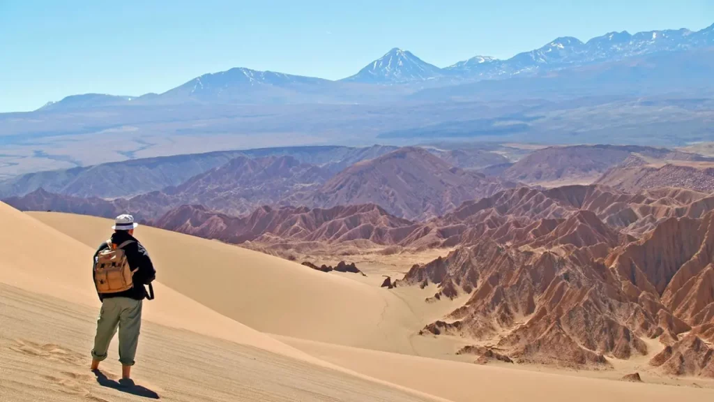 Turista em uma duna no deserto do Atacama, admirando a vista das montanhas e formações rochosas do Valle de la Luna sob céu claro.