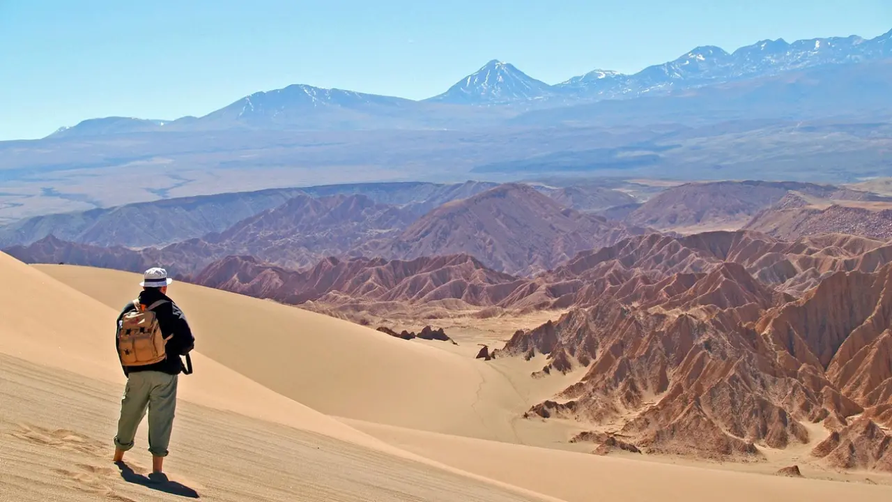 Turista em uma duna no deserto do Atacama, admirando a vista das montanhas e formações rochosas do Valle de la Luna sob céu claro.