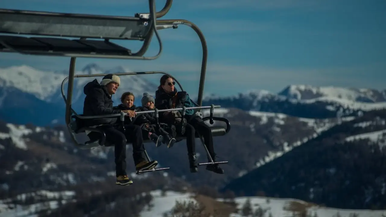 Familia disfrutando de un paseo en telesilla en una estación de esquí, rodeada de montañas nevadas bajo un cielo azul.