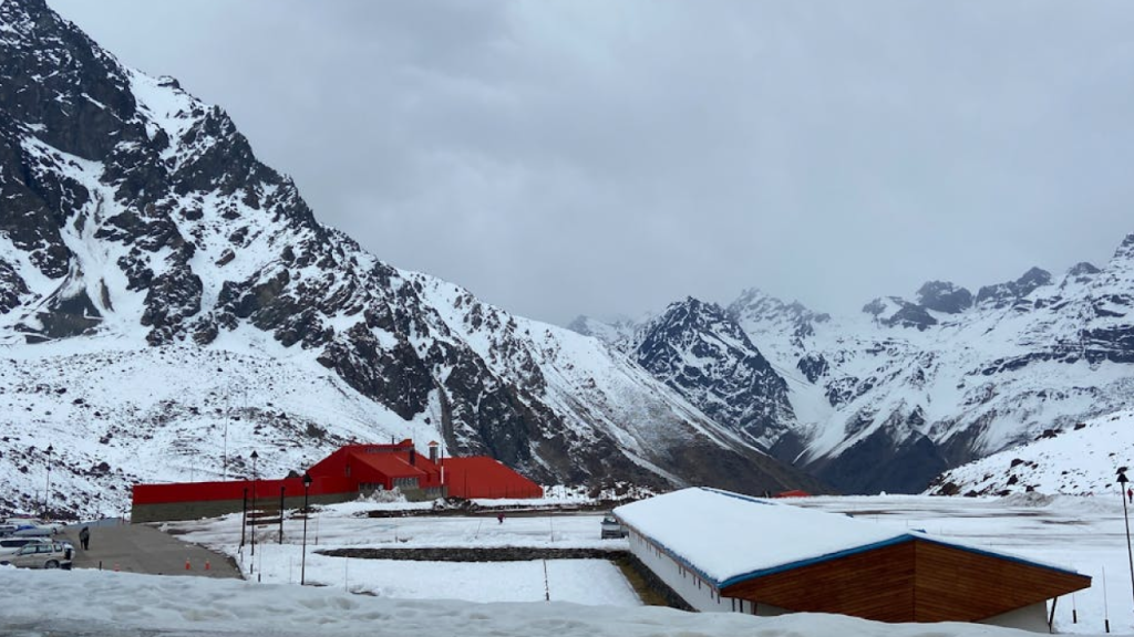 Chalé de telhado vermelho aos pés de montanha andina nevada — cenário clássico para conhecer a neve no Chile.