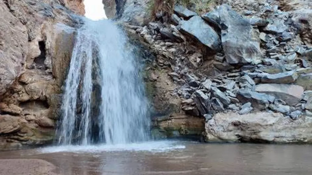 Cachoeira Escondida no Deserto do Atacama com queda d'água cercada por rochas áridas, formando um pequeno poço natural.
