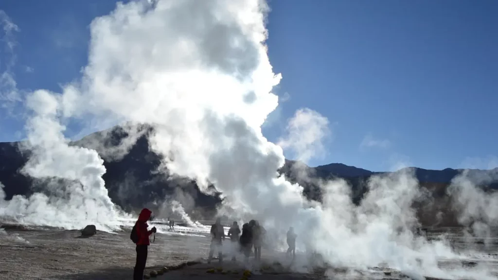 Grupo de turistas próximos aos Gêiseres del Tatio no Atacama, envoltos por colunas de vapor em uma manhã fria nas montanhas.