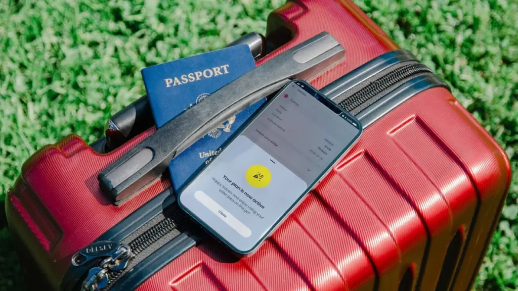 Passaporte, mala de viagem e celular com chip de internet ativado, simbolizando preparo para uma viagem internacional segura.