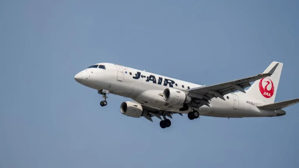 Avião da companhia J-AIR se aproximando para pouso com céu azul ao fundo.
