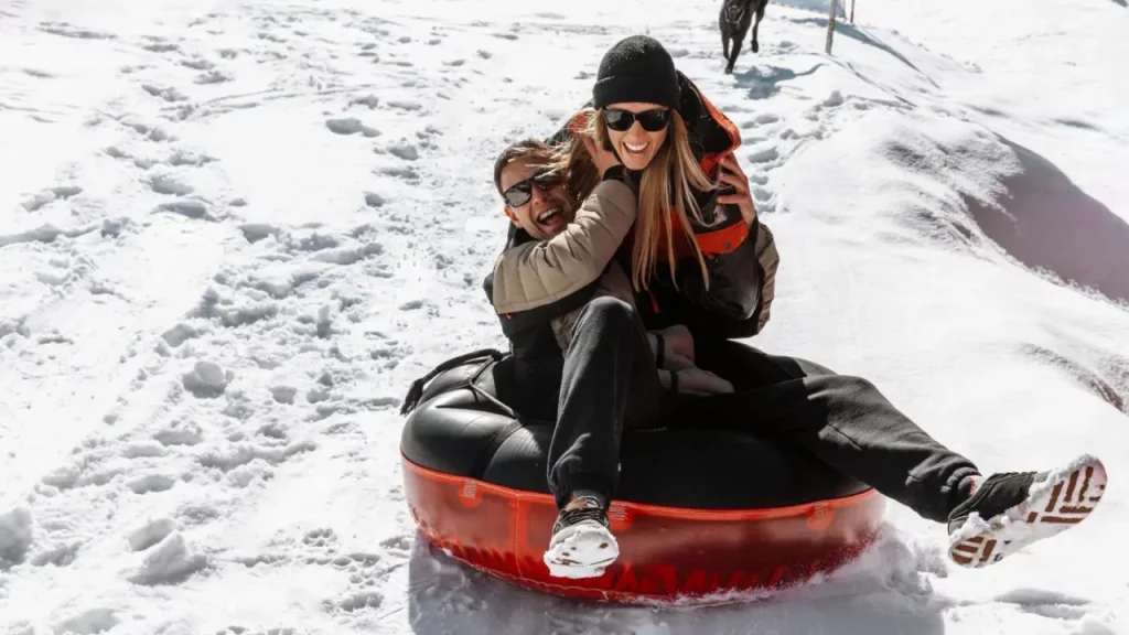 Casal sorridente curtindo a neve em uma bóia inflável nas montanhas do Chile.