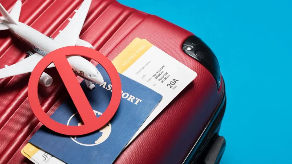 Símbolo de prohibición sobre pasaporte, tarjeta de embarque y avión de juguete encima de una maleta roja, representando restricciones de viaje.