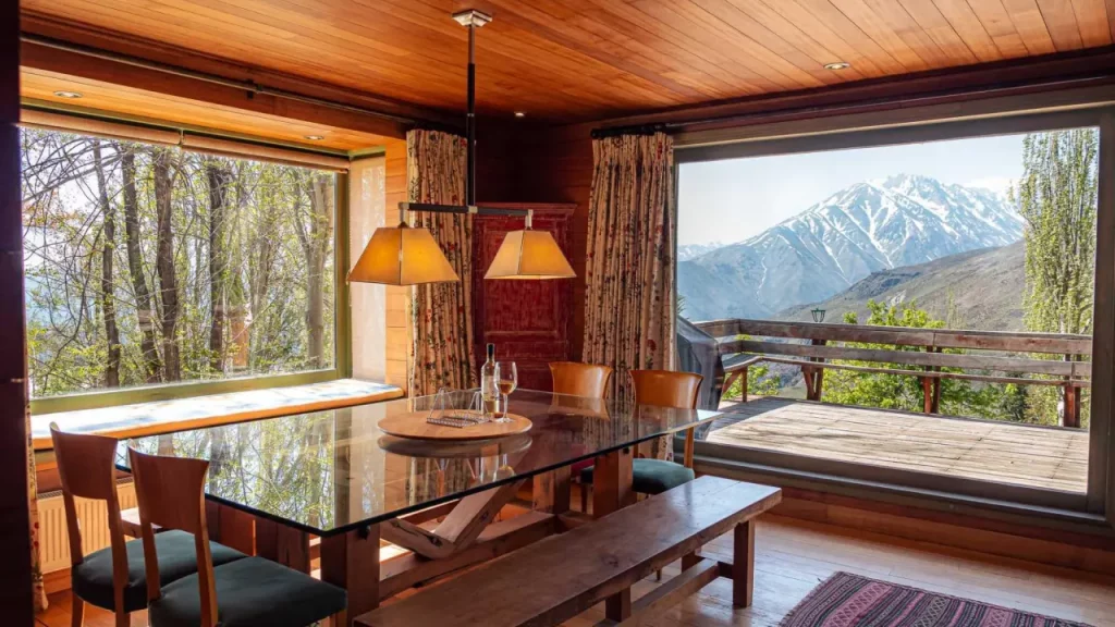 Sala de jantar com janelas amplas e vista panorâmica para a Cordilheira dos Andes, na Casa Condor, hostel em Farellones, Chile.